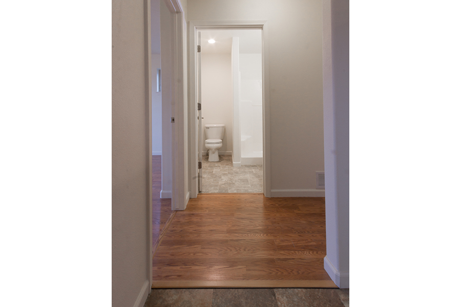 A first-floor bathroom with a white shower sits off a wide entryway that also leads to a bedroom.